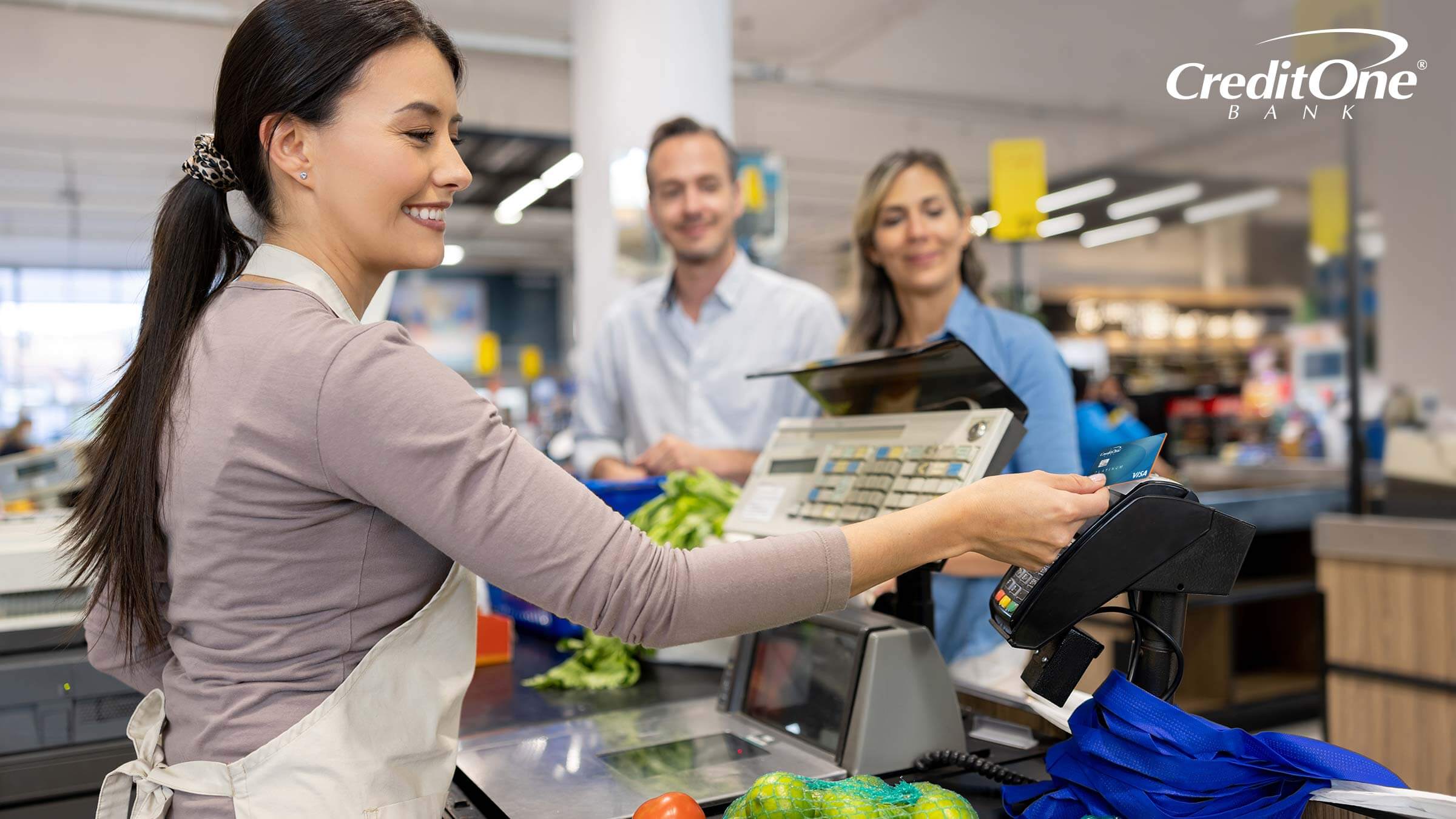 A cashier runs a credit card for a couple buying groceries, triggering a grocery merchant category code